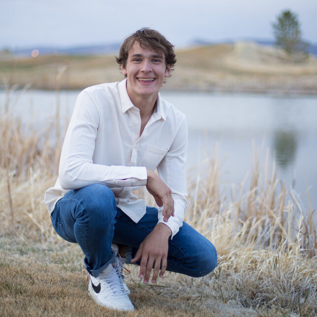 Young man in white shirt kneeling near lake